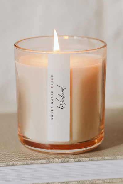 Candle in a glass jar labeled 'Weekend' on a stack of books with a blurred background