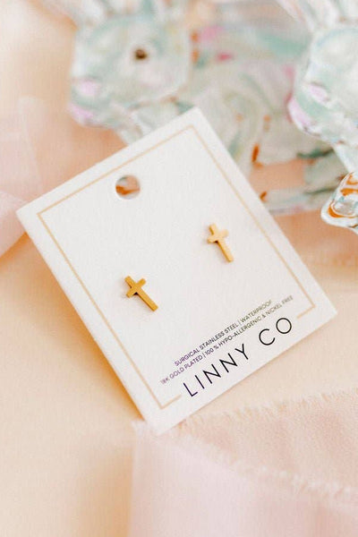 Gold cross earrings on a LINNY CO card with a soft pink background