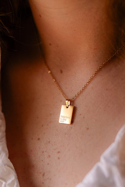 Close-up of a person wearing a gold necklace with a rectangular pendant.