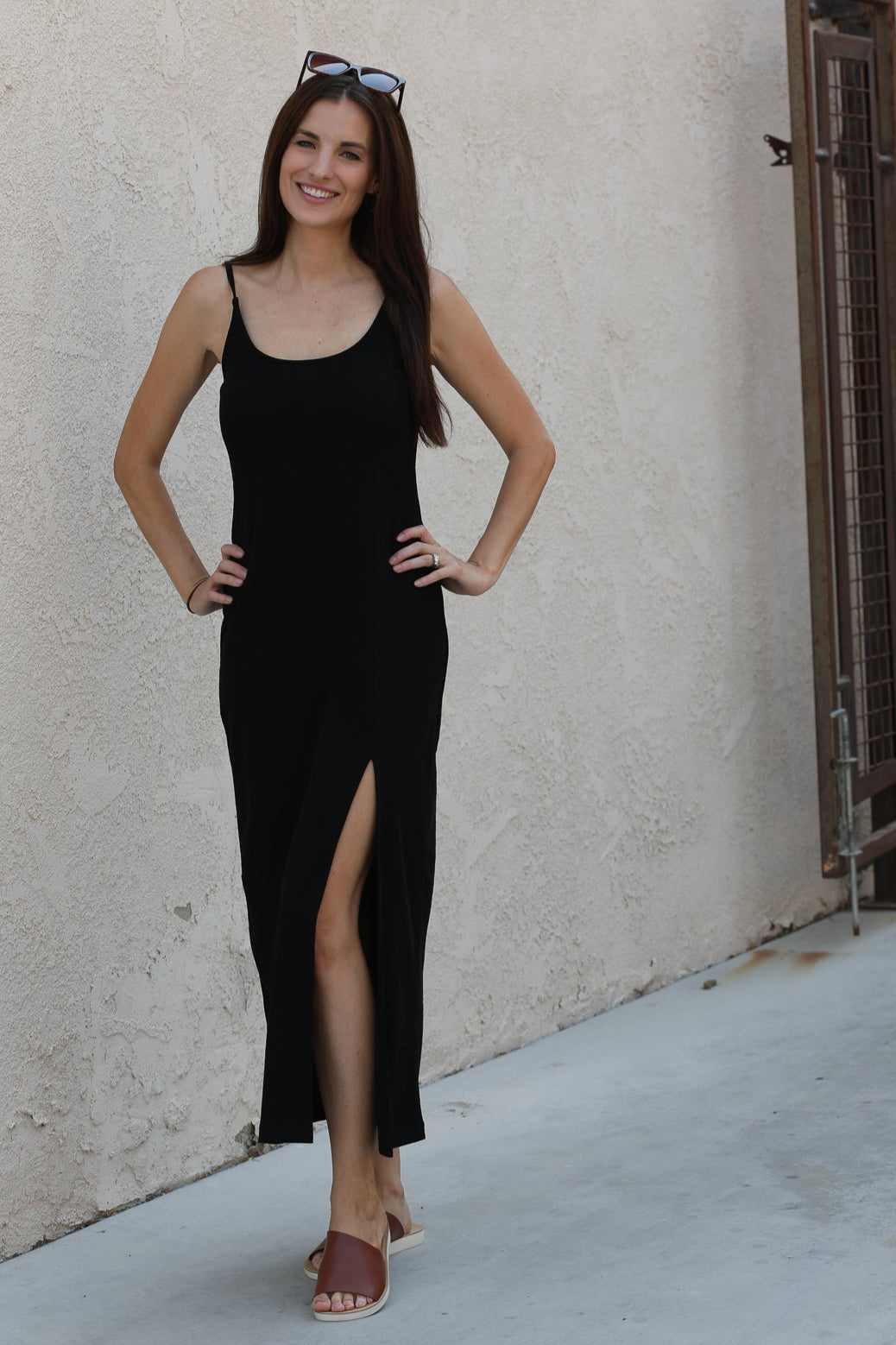 Woman in a black dress standing against a beige wall.