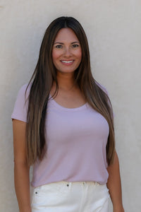 Woman wearing a light purple shirt and white pants against a beige wall