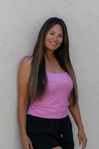 Woman wearing a pink top and black pants against a beige wall