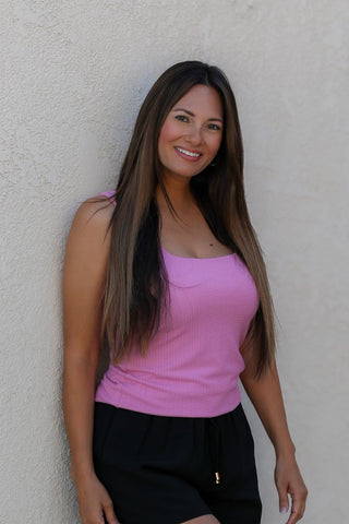 Woman wearing a pink top and black pants against a beige wall