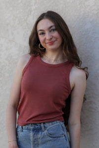 Woman wearing a red tank top and denim shorts against a beige wall