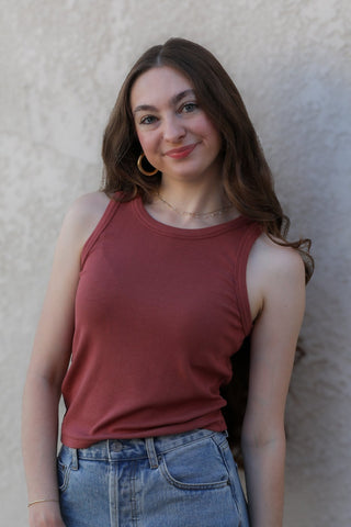 Woman wearing a red tank top and denim shorts against a beige wall