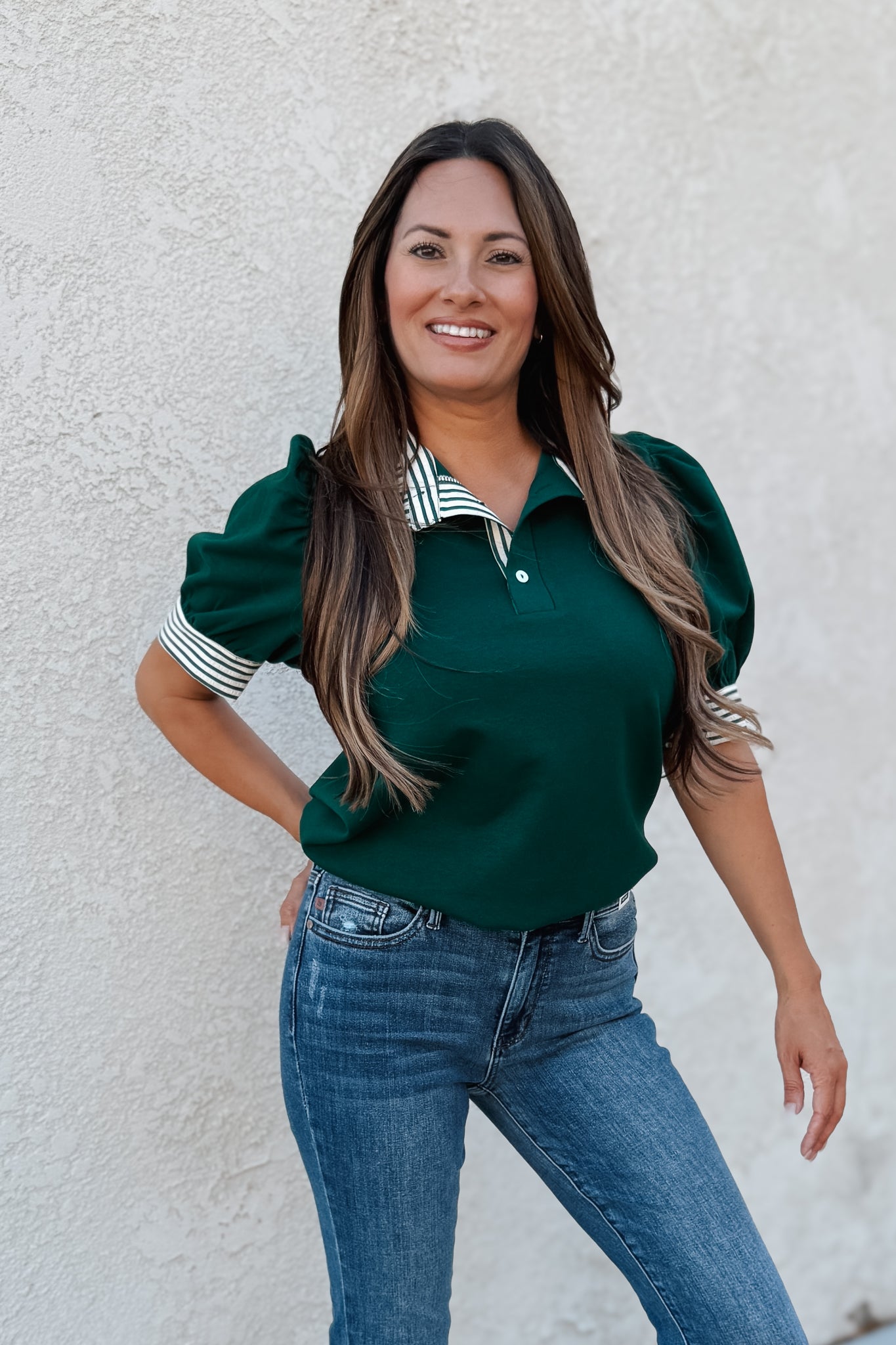 Woman wearing a green top with puffed sleeves and blue jeans against a white wall