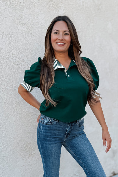 Woman wearing a green top with puffed sleeves and blue jeans against a white wall