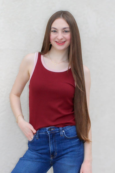 Woman wearing a red tank top and blue jeans against a light gray wall.