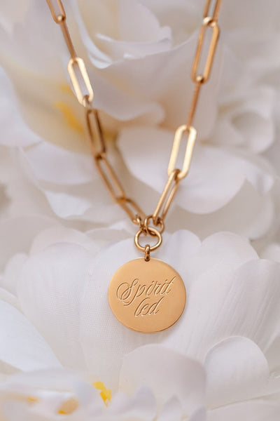 Gold necklace with a round pendant on a white floral background