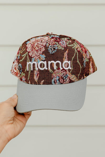 Floral-patterned cap with 'mama' text held by a hand against a neutral background