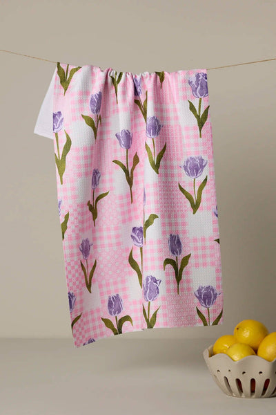 Towel with tulip pattern on a pink checkered background hanging on a line, with a bowl of lemons below.