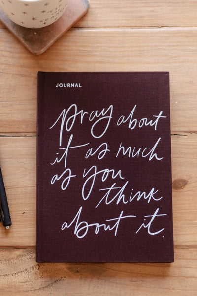 Journal with motivational quote on a wooden surface with a pen and mug.