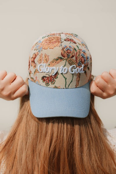 Person wearing a floral-patterned cap with 'Glow to God' text on a neutral background