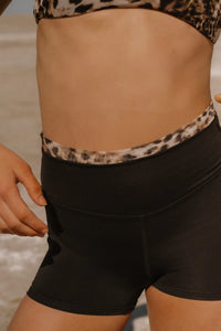 Person wearing a leopard print top and black shorts on a beach.
