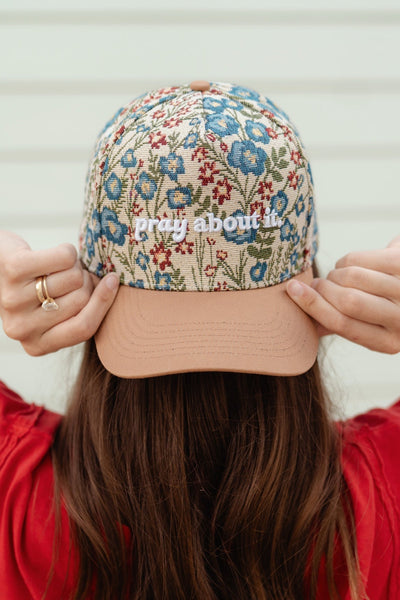 Person wearing a floral-patterned cap with 'pray about it' text, against a neutral background