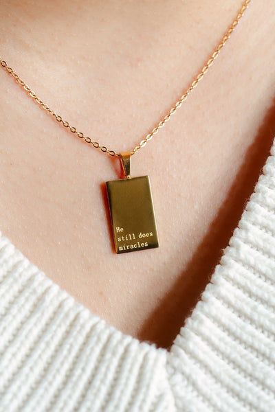Gold necklace with a pendant on a person wearing a white sweater
