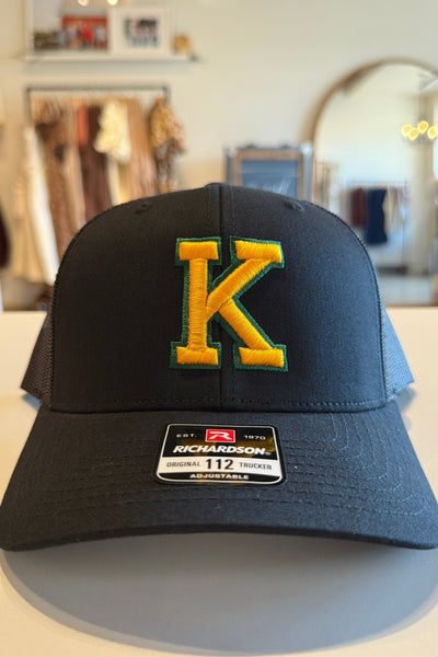 Black cap with yellow 'K' logo on a white surface