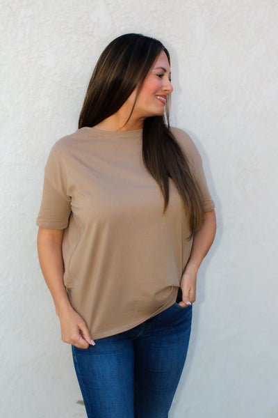 Woman wearing a beige top and blue jeans against a white wall