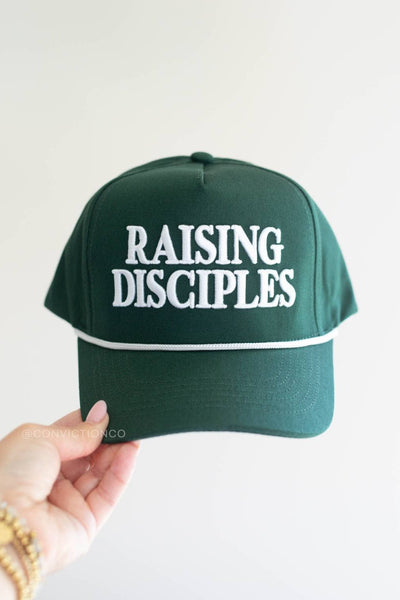 Green cap with 'RAISING DISCIPLES' text held by a hand on a light background