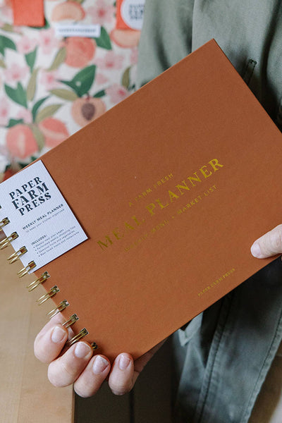 Person holding a brown planner with 'Paper + Press' branding.