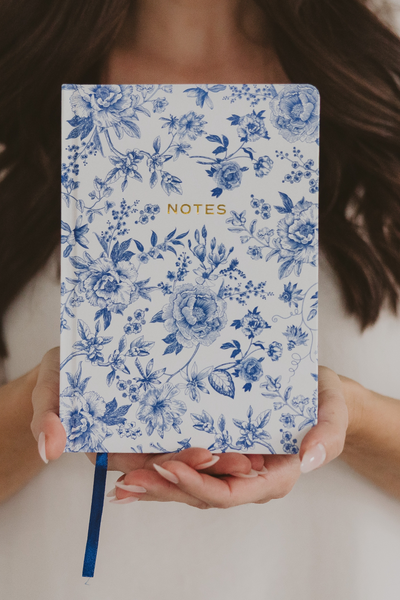 Person holding a blue floral notebook with 'NOTES' text